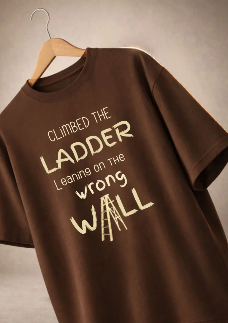 Brown oversized t-shirt with cream typography print reading "Climbed The Ladder Leaning On The Wrong Wall" hanging on a wooden hanger
