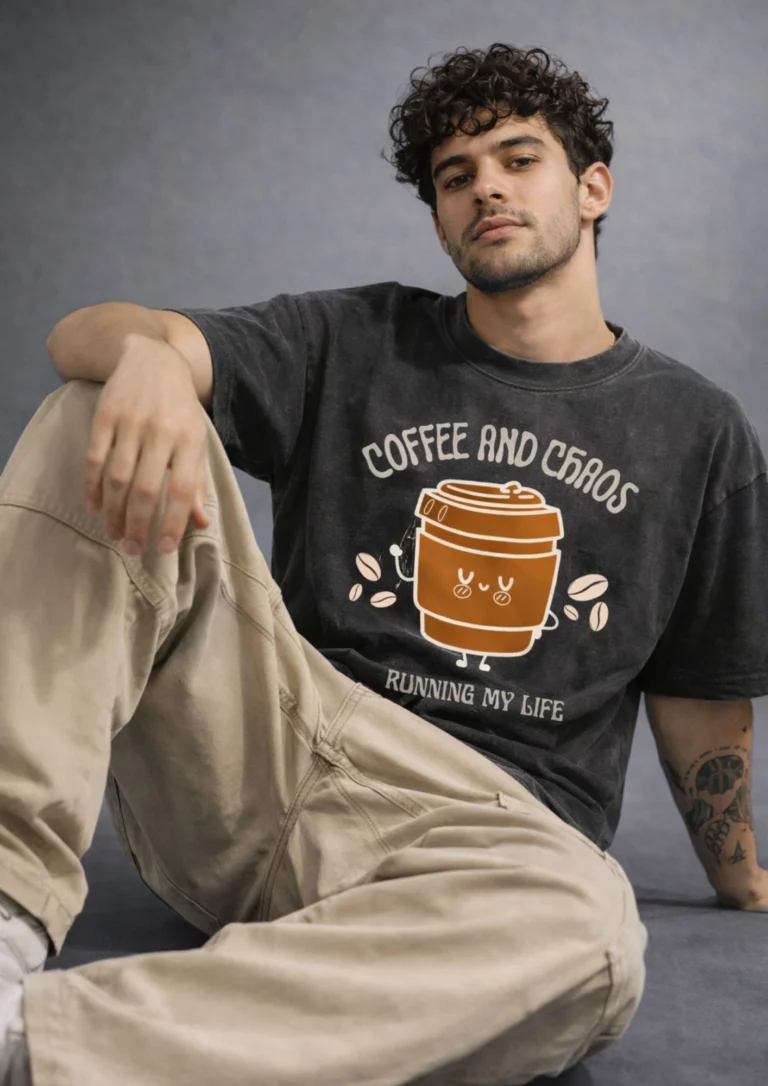 Acid wash black oversized t-shirt with a cute kawaii coffee cup graphic and text reading "Coffee And Chaos Running My Life" hanging on a wooden hanger against a grey background